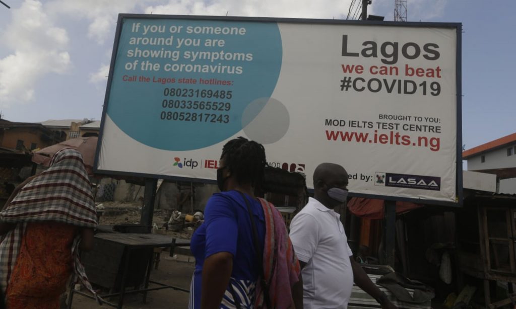 Pedestrians walk past a sign telling residents to call phone numbers if they have symptoms of COVID-19, the disease caused by the coronavirus, in Lagos, Nigeria, May 12, 2020.