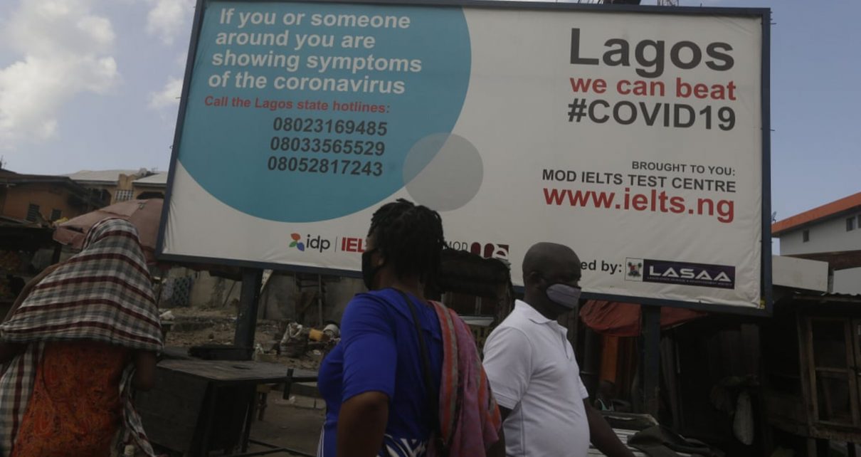 Pedestrians walk past a sign telling residents to call phone numbers if they have symptoms of COVID-19, the disease caused by the coronavirus, in Lagos, Nigeria, May 12, 2020.